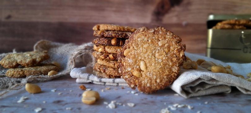Biscuits croustillants aux pois chiches et à la cacahuète disposés sur un torchon devant une boîte métallique dorée